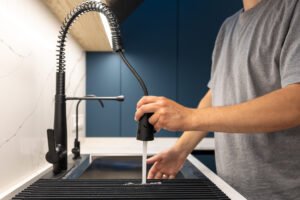 man rinsing dish rack with pullout sprayer by the sink. flow control.